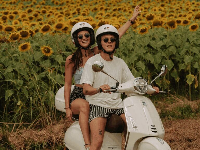 Couple on a white Vespa primavera with sunflowers in the background